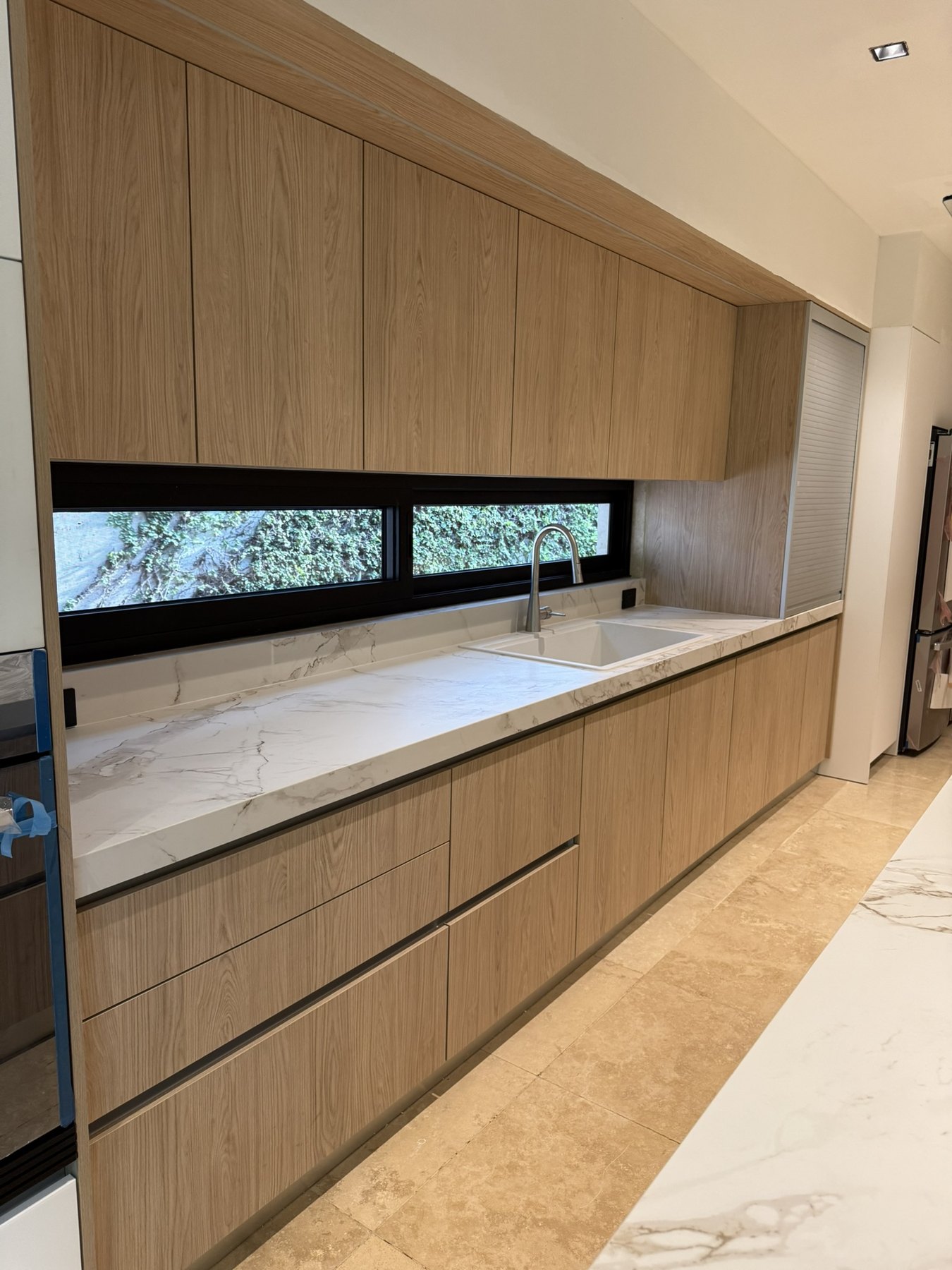 Cocina Novecci de madera clara con cubierta de piedra y ventana horizontal